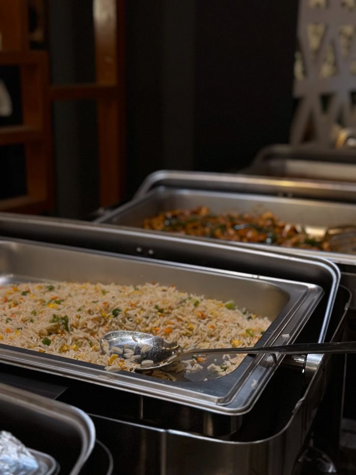 A close-up of buffet-style rice and vegetables served in catering trays, ready for guests.