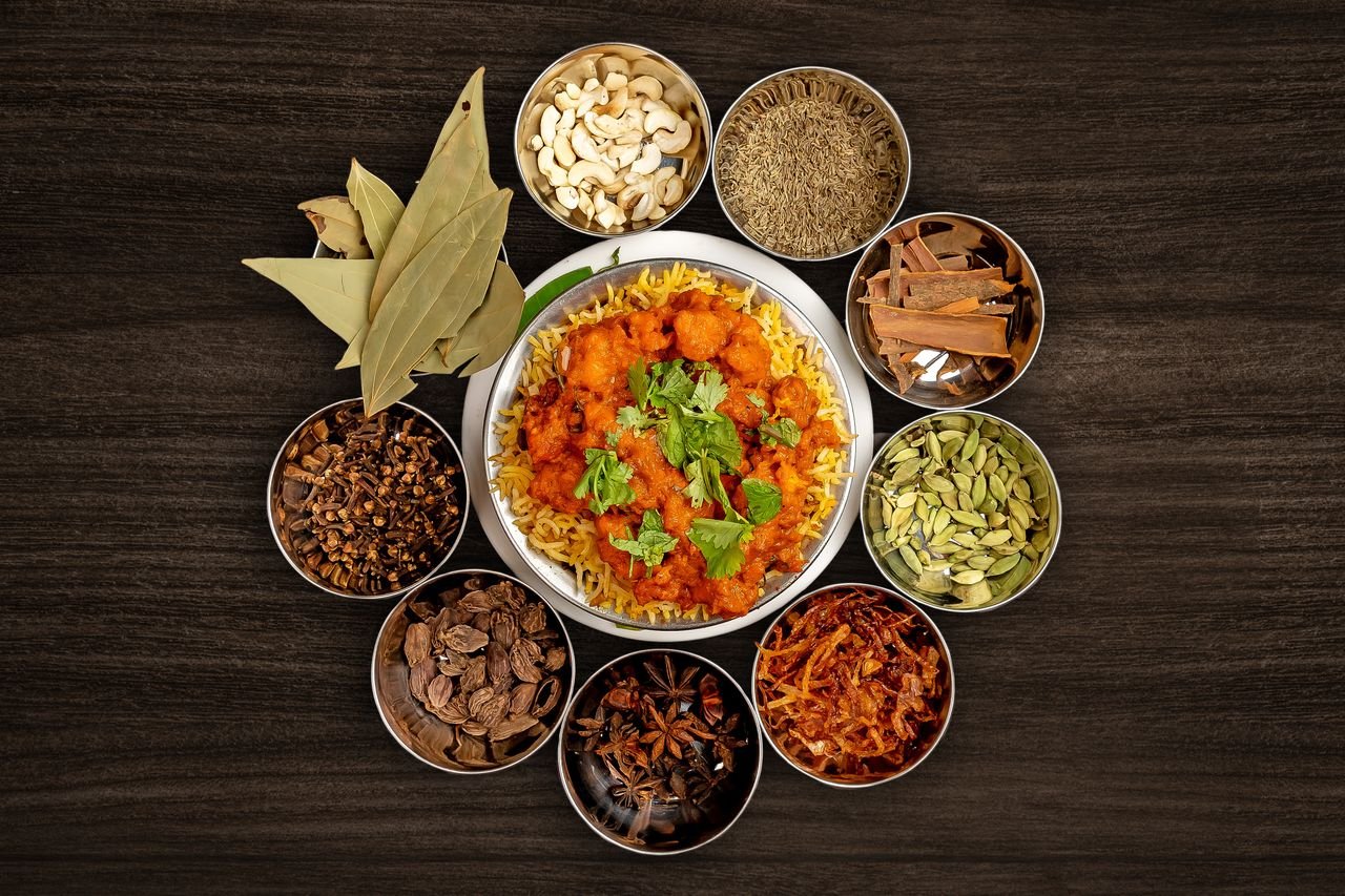 Delicious biryani surrounded by vibrant Indian spices on a dark wooden table.
