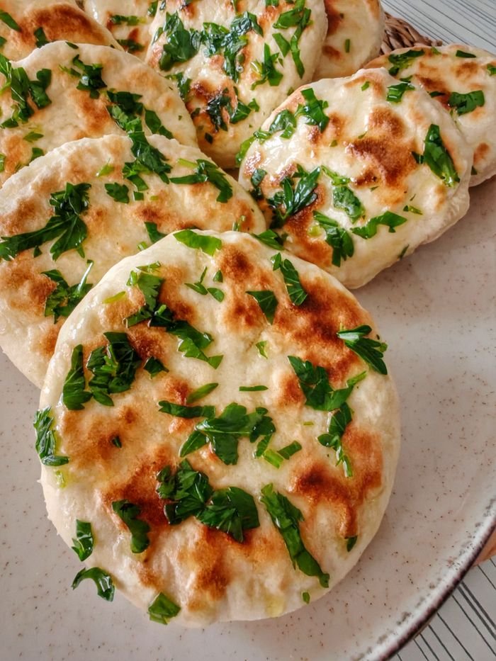 Freshly baked naan bread garnished with parsley on a plate, ready to eat.